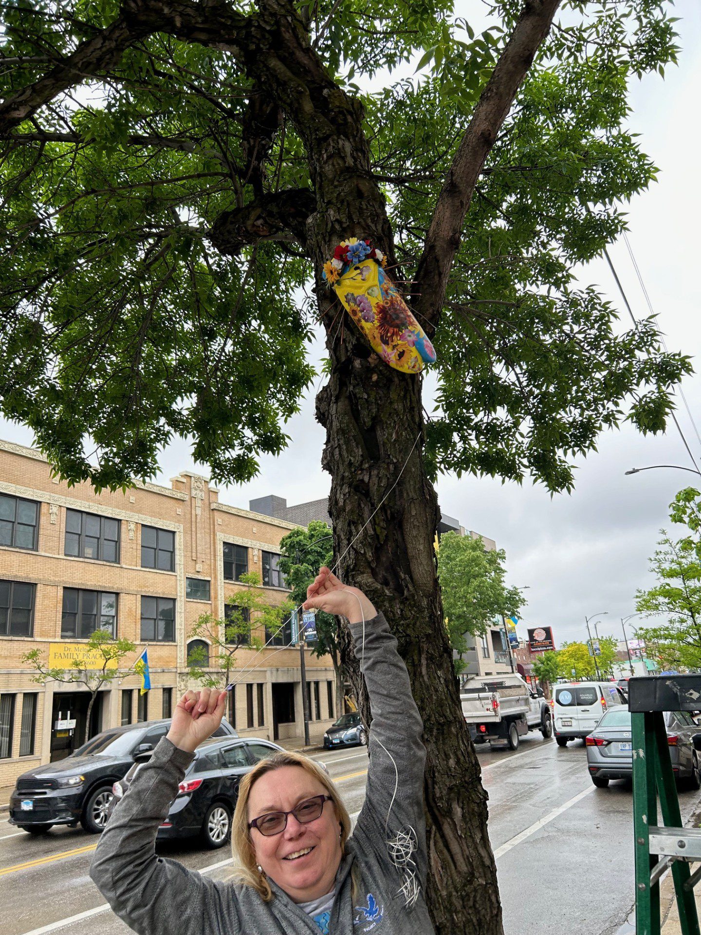 67cf41f34cfeb_Cicada project 2024 A woman is hanging up a skateboard on the tree.