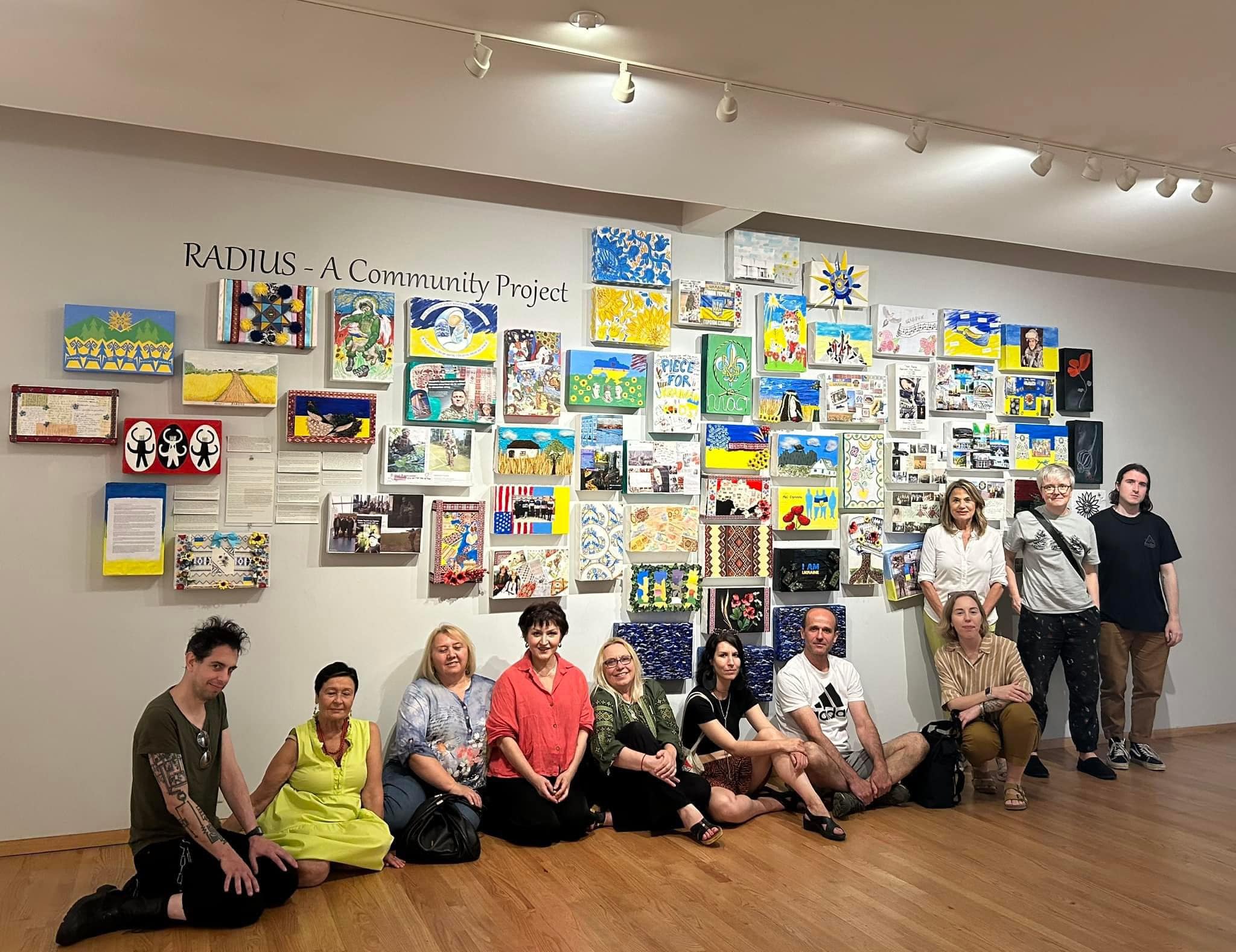 67cf41f397ef0_Radius (e4f2cada-c3e6-48bf-840b-0f50f9791053) A group of people sitting on the floor in front of a wall covered with paintings.