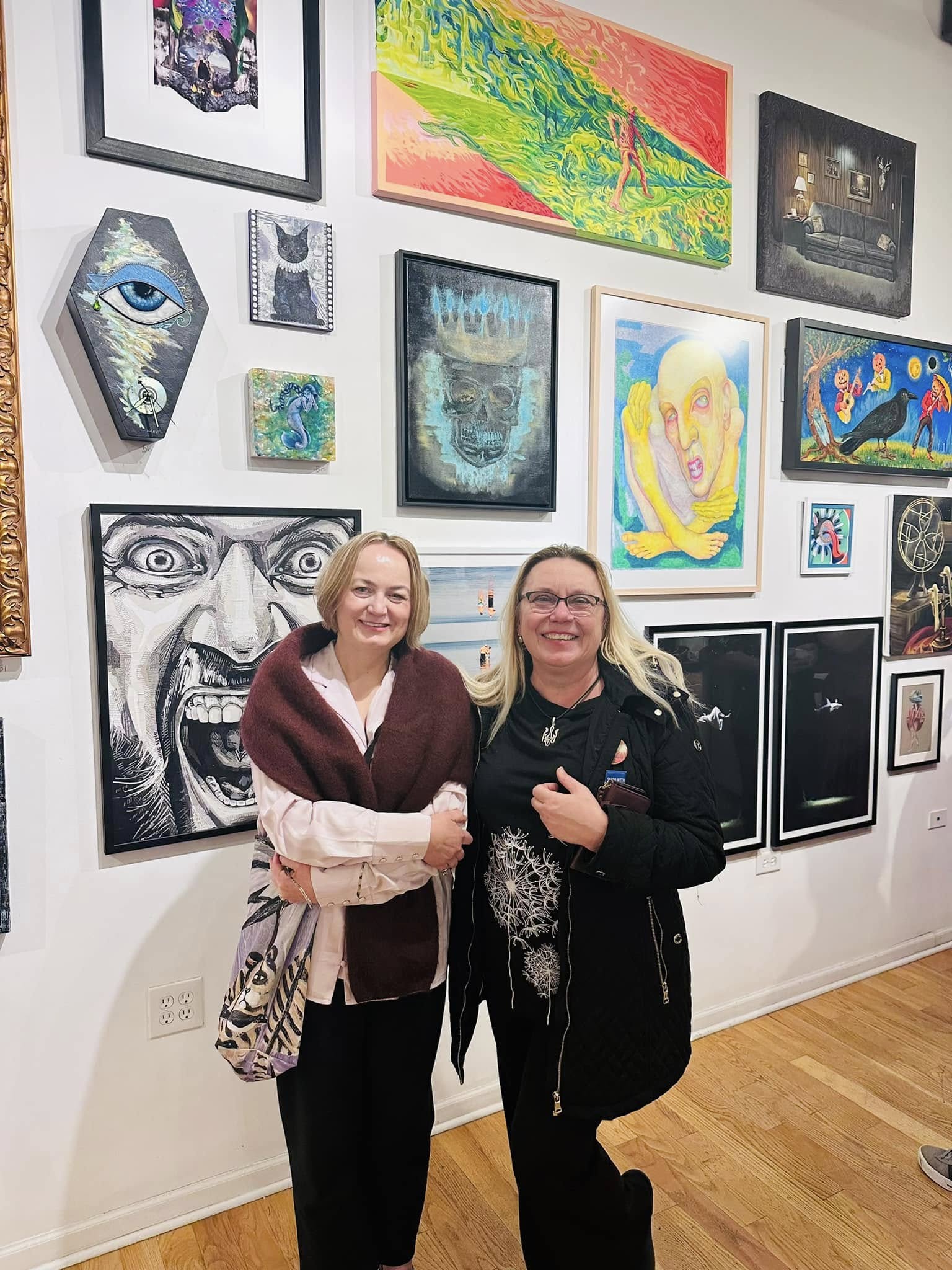 Two women standing in front of a wall with many paintings on it.